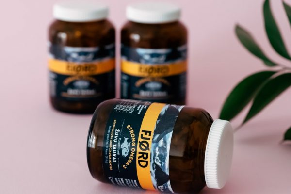 Amber vitamin bottles with a leafy accent on a pink surface, evoking wellness.