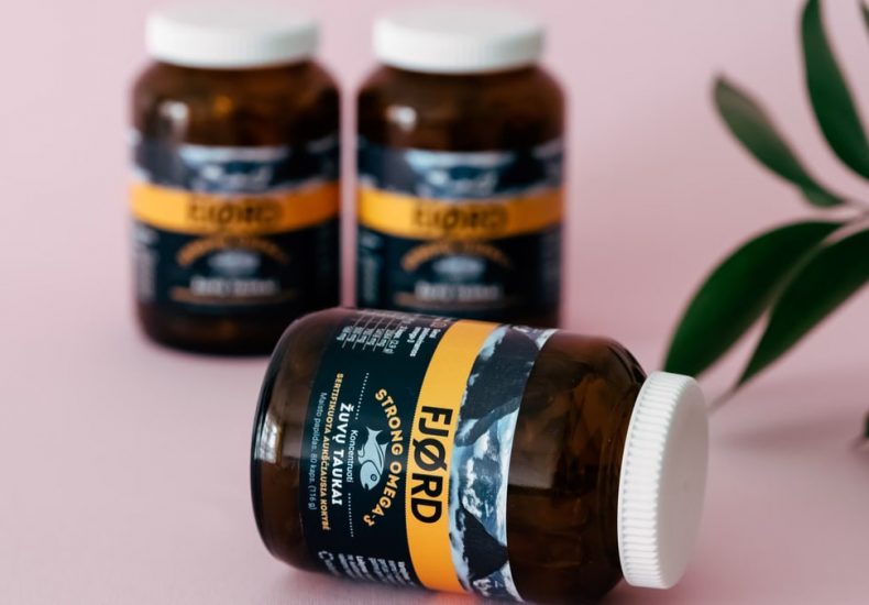 Amber vitamin bottles with a leafy accent on a pink surface, evoking wellness.